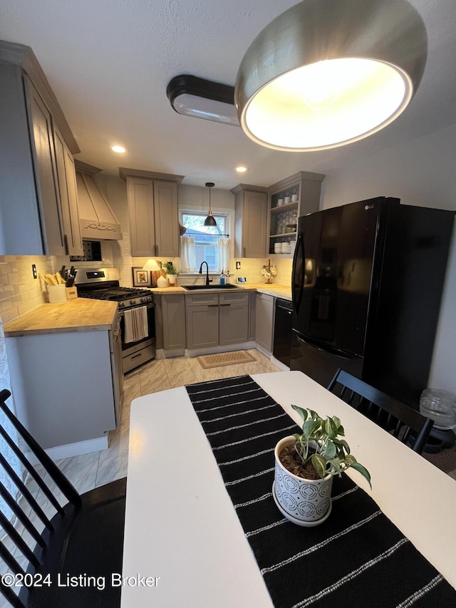 kitchen with sink, butcher block countertops, pendant lighting, black appliances, and custom exhaust hood