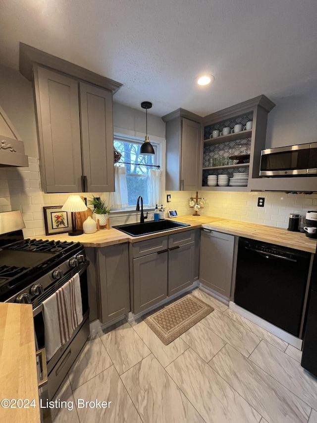 kitchen featuring backsplash, sink, appliances with stainless steel finishes, decorative light fixtures, and butcher block counters