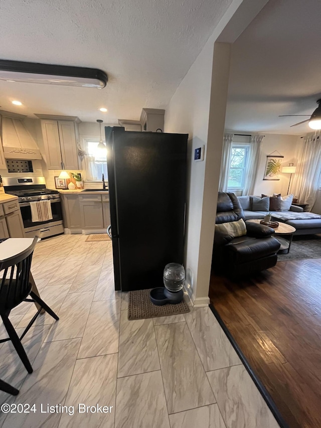 kitchen with ceiling fan, sink, black fridge, stainless steel stove, and custom exhaust hood