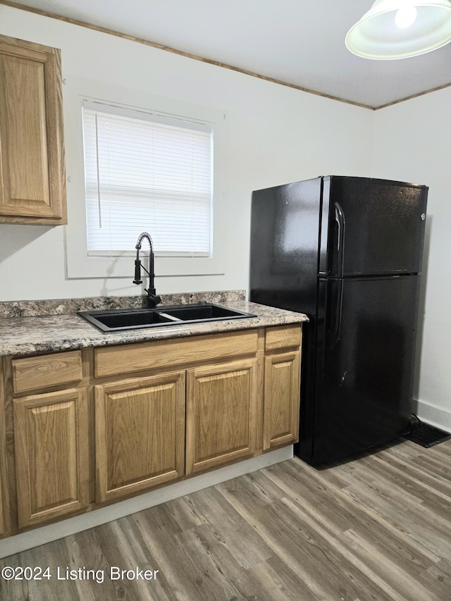 kitchen with black fridge, wood-type flooring, sink, and ornamental molding