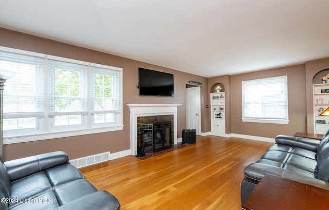 living room featuring a tile fireplace, built in shelves, and hardwood / wood-style flooring