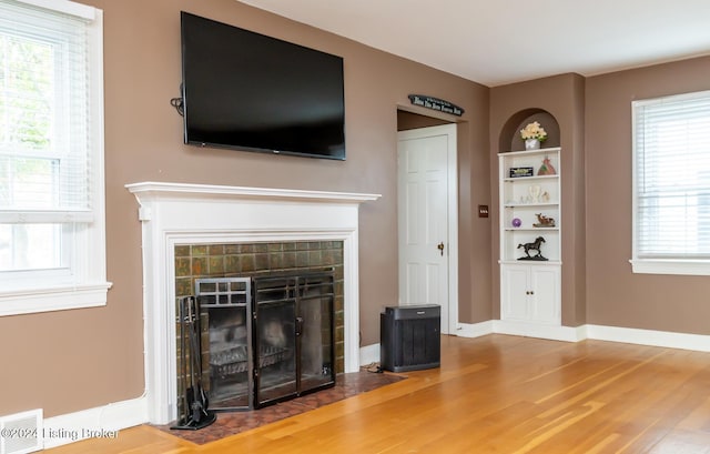 unfurnished living room with wood-type flooring, built in features, and plenty of natural light