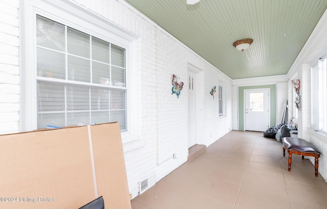 corridor featuring light tile patterned flooring and brick wall