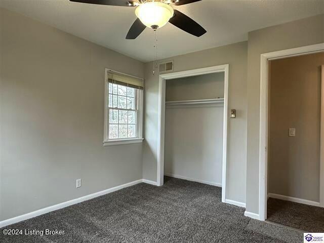 unfurnished bedroom featuring dark colored carpet, a closet, and ceiling fan