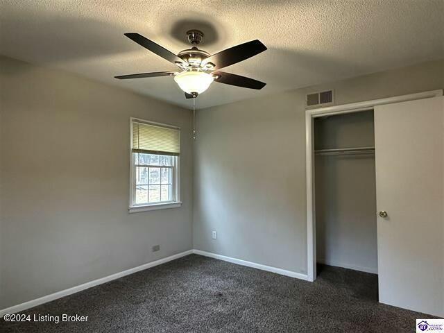 unfurnished bedroom with ceiling fan, a closet, a textured ceiling, and dark colored carpet