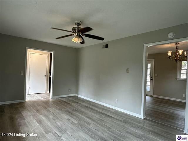 empty room with hardwood / wood-style floors and ceiling fan with notable chandelier