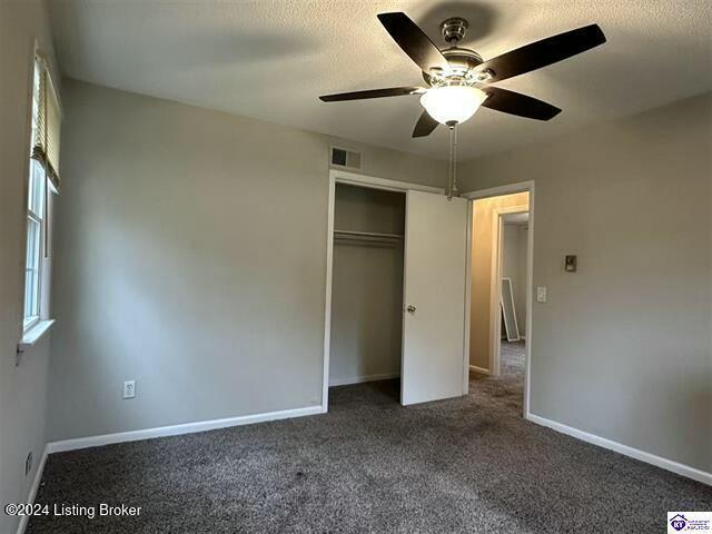 unfurnished bedroom featuring ceiling fan, a closet, and dark carpet