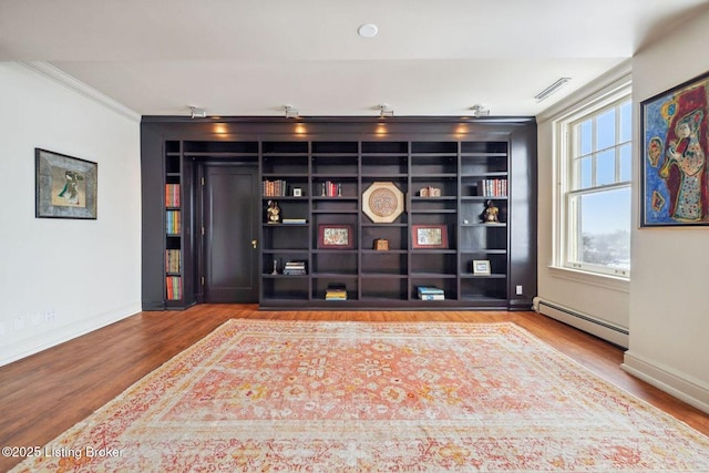 cinema featuring built in shelves, hardwood / wood-style floors, crown molding, and a baseboard radiator