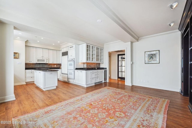 kitchen with light hardwood / wood-style floors, backsplash, white appliances, a kitchen island, and white cabinets