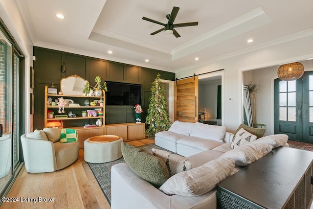 living room featuring a barn door, crown molding, light hardwood / wood-style flooring, and a tray ceiling