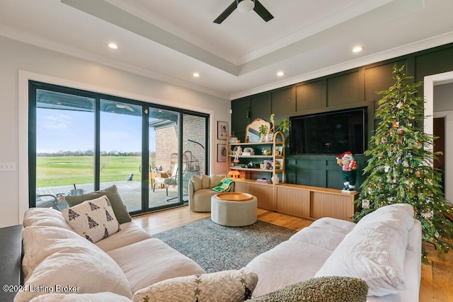 living room featuring ceiling fan, a raised ceiling, crown molding, and light hardwood / wood-style flooring