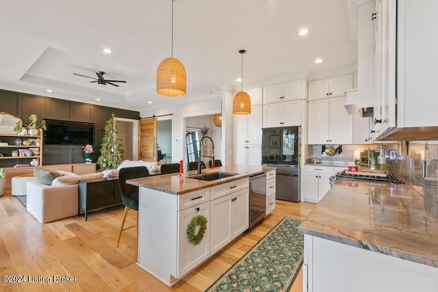 kitchen with a kitchen island with sink, hanging light fixtures, sink, a barn door, and white cabinetry