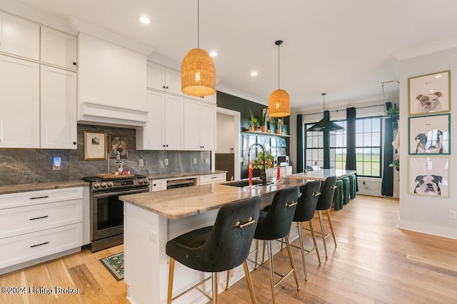 kitchen with stainless steel range, a center island with sink, hanging light fixtures, and sink