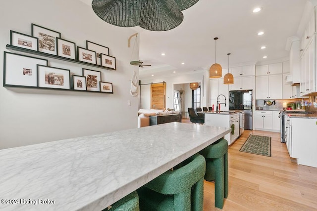 kitchen featuring ceiling fan, pendant lighting, white cabinets, stainless steel stove, and an island with sink