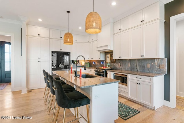 kitchen with white cabinetry, black microwave, a kitchen island with sink, and sink