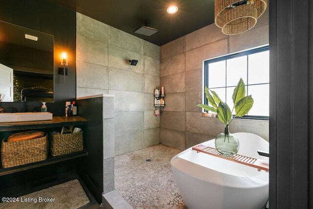 bathroom with a bath, tile walls, and sink