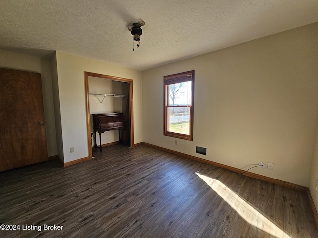 unfurnished bedroom with a textured ceiling, dark hardwood / wood-style floors, and a closet