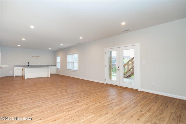 unfurnished living room featuring sink, light hardwood / wood-style floors, and french doors