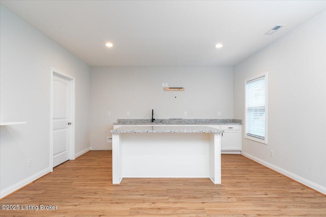 kitchen with a kitchen island, light stone counters, white cabinetry, and light wood-type flooring