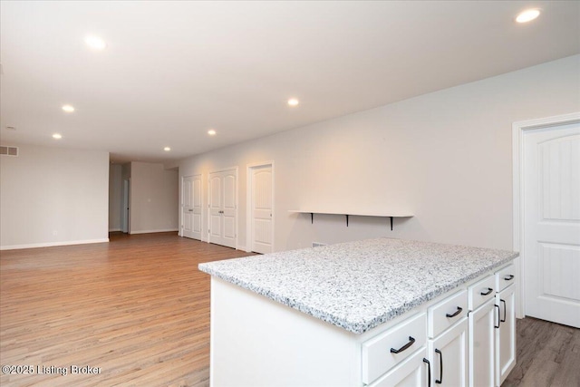 kitchen featuring white cabinetry, a center island, light stone countertops, and light hardwood / wood-style flooring