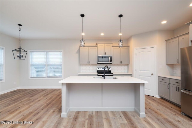 kitchen with appliances with stainless steel finishes, decorative light fixtures, a kitchen island with sink, and sink