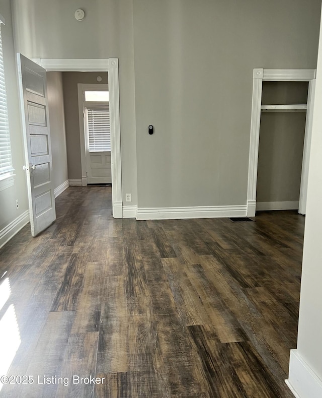 unfurnished bedroom featuring dark wood-type flooring, a closet, and baseboards