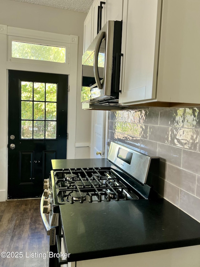 kitchen featuring a textured ceiling, dark wood-type flooring, white cabinets, appliances with stainless steel finishes, and tasteful backsplash