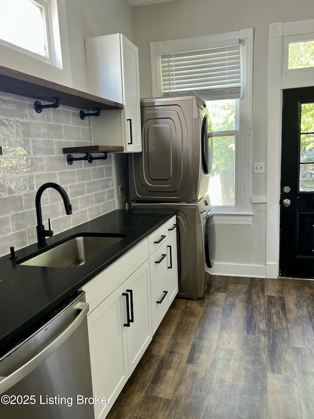 clothes washing area featuring a healthy amount of sunlight, dark wood finished floors, a sink, and stacked washer and clothes dryer