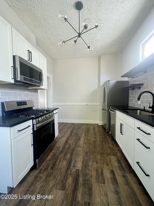 kitchen featuring a sink, appliances with stainless steel finishes, dark wood-style floors, open shelves, and dark countertops