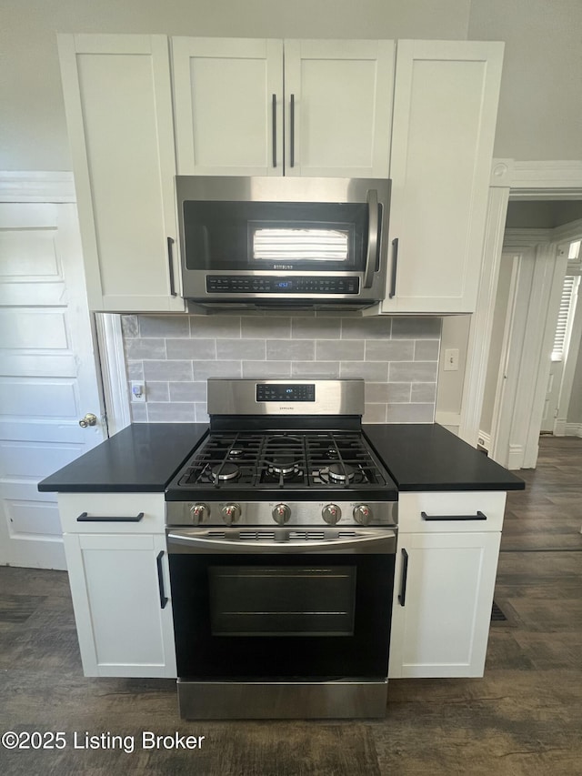 kitchen featuring dark wood-style floors, stainless steel appliances, dark countertops, decorative backsplash, and white cabinetry