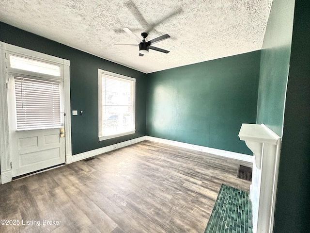 interior space featuring a ceiling fan, a textured ceiling, baseboards, and wood finished floors