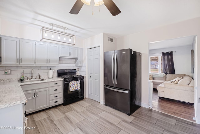 kitchen featuring ceiling fan, sink, black gas range oven, tasteful backsplash, and stainless steel fridge