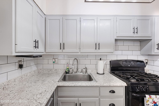 kitchen with tasteful backsplash, light stone counters, sink, black gas stove, and white cabinetry