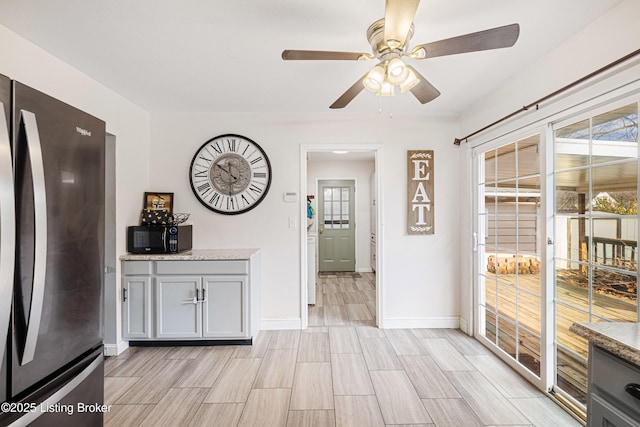 interior space featuring gray cabinetry, stainless steel fridge, ceiling fan, and light stone counters