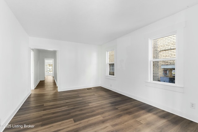 empty room with visible vents, dark wood-type flooring, and baseboards