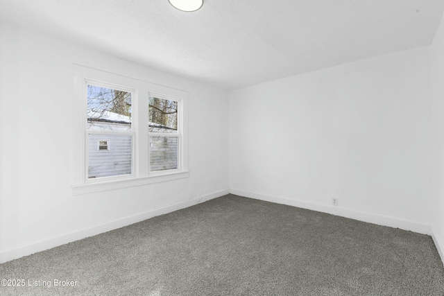 spare room featuring baseboards and dark carpet