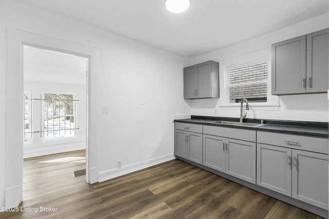 kitchen with a sink, dark countertops, gray cabinetry, and dark wood finished floors