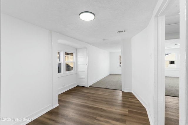 unfurnished room with dark wood-type flooring, baseboards, visible vents, and a textured ceiling