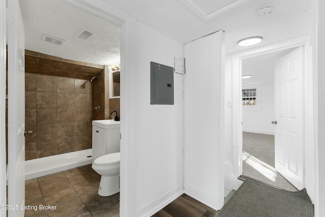 bathroom featuring tiled shower, toilet, a textured ceiling, vanity, and electric panel