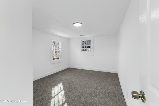 spare room featuring dark colored carpet, visible vents, and baseboards