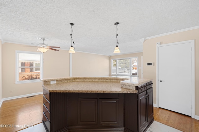 kitchen featuring dark brown cabinets, a center island, crown molding, and decorative light fixtures