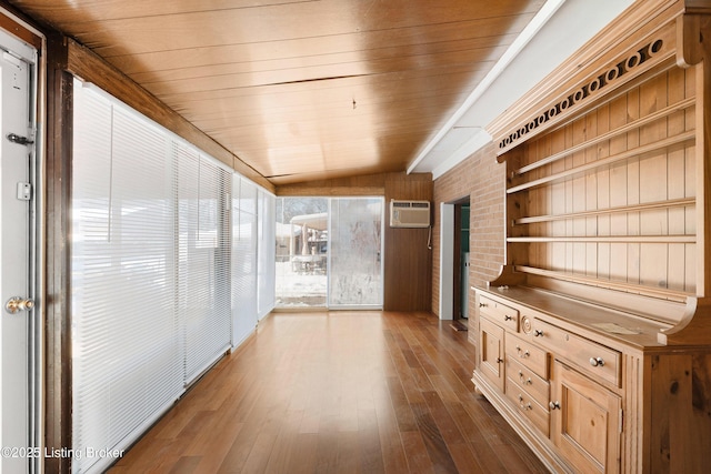 interior space featuring a wall unit AC, wood walls, wood-type flooring, vaulted ceiling, and wood ceiling