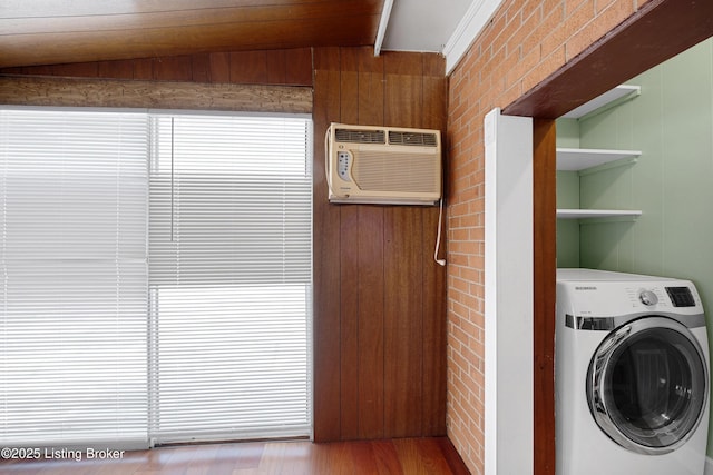 laundry area with brick wall, a wall unit AC, hardwood / wood-style floors, washer / dryer, and wooden walls