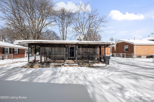 snow covered rear of property with a sunroom