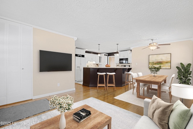 living room with a textured ceiling, ceiling fan, light hardwood / wood-style floors, and crown molding