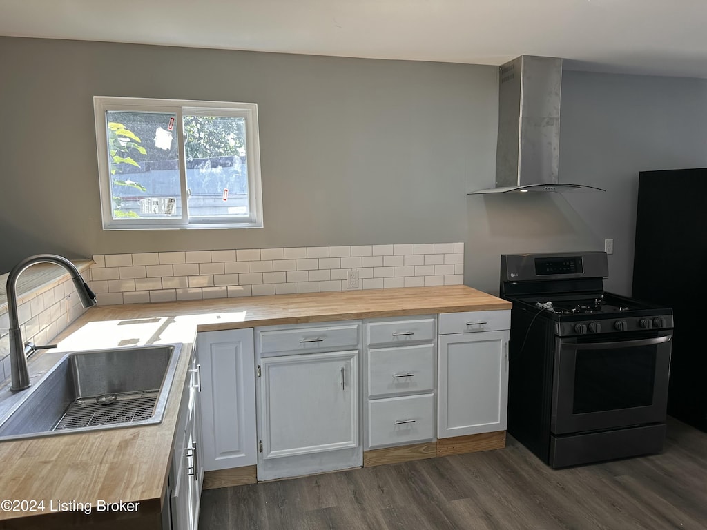 kitchen with wood counters, white cabinets, sink, wall chimney exhaust hood, and stainless steel range with gas stovetop