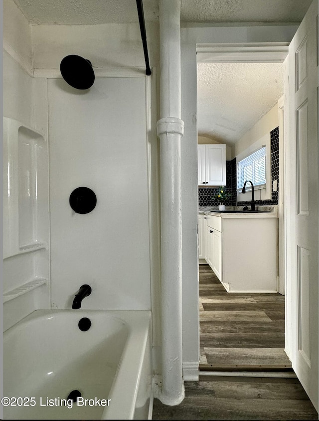 bathroom featuring tasteful backsplash, wood-type flooring, a textured ceiling,  shower combination, and vanity