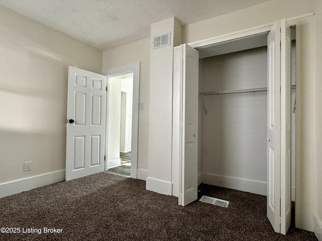 unfurnished bedroom with a textured ceiling, dark carpet, and a closet