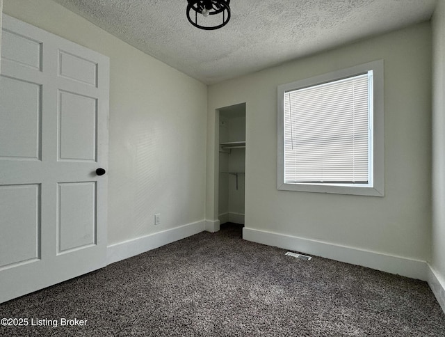 unfurnished bedroom with a textured ceiling, dark carpet, and a closet