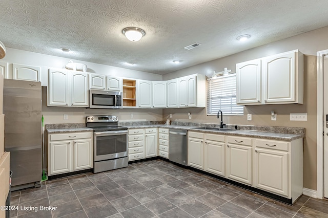 kitchen featuring appliances with stainless steel finishes, a textured ceiling, white cabinetry, and sink